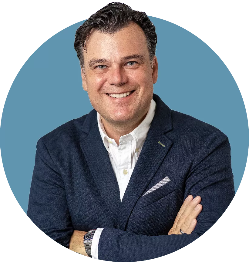 Porträt von Robert Käß, Aufsichtsrat der audius SE, lächelnd in dunklem Sakko und weißem Hemd vor blauem Hintergrund.