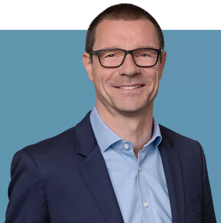 Porträt von Matthias Kraft, Vorstandsmitglied der audius SE, lächelnd in dunklem Sakko und blauem Hemd vor blauem Hintergrund.